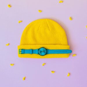 Fashionable flat lay set with yellow beanie hat and blue watches among mini bananas